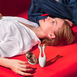 "White RF facial device with gold accents, placed beside a woman lying on a red surface, wearing a white blouse."