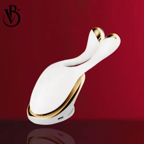 White RF facial device with a sleek ergonomic design, gold accents on the handles, set against a red background.