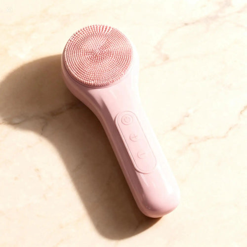 "Pink sonic facial cleansing brush with textured silicone head and control buttons, angled view on a light surface."