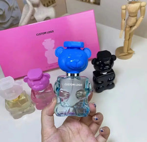 "Colorful toy bear perfume bottles in various shades, held in hand with pink box in background."