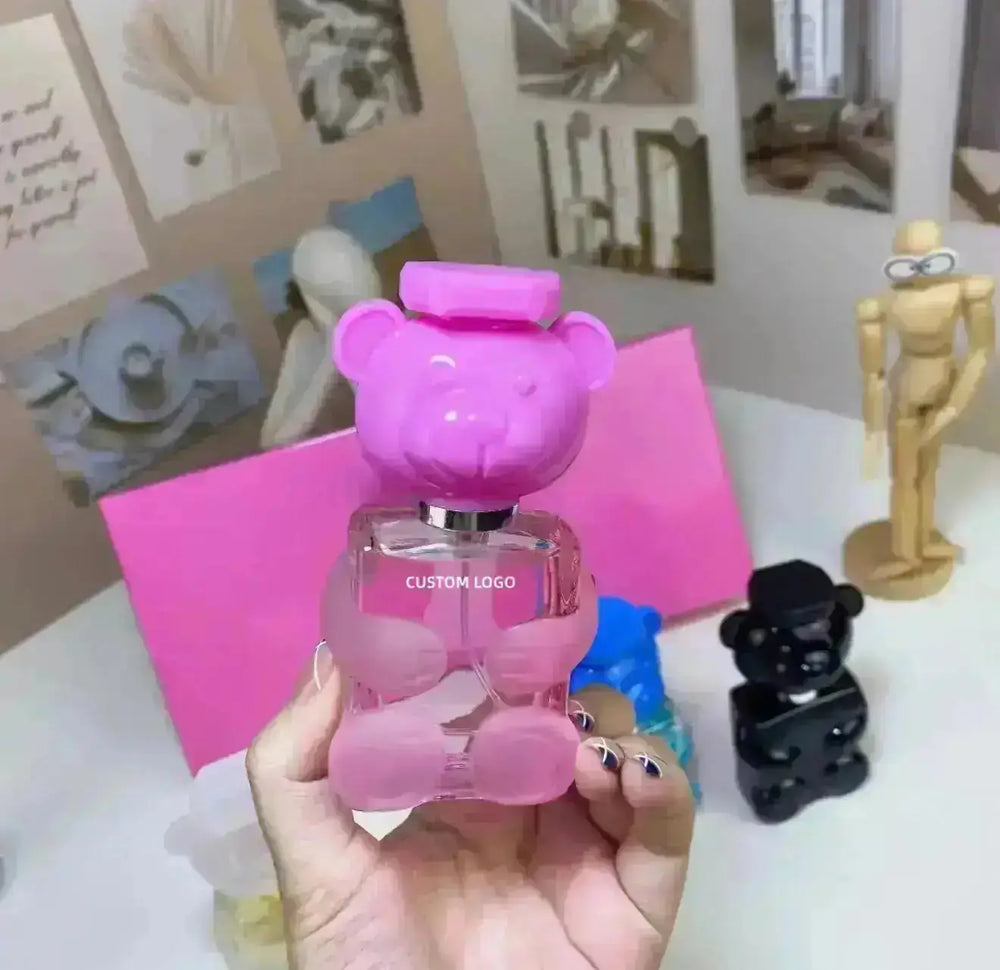 "Pink bear-shaped perfume bottle with a square cap, held in hand, surrounded by other colorful bear bottles."