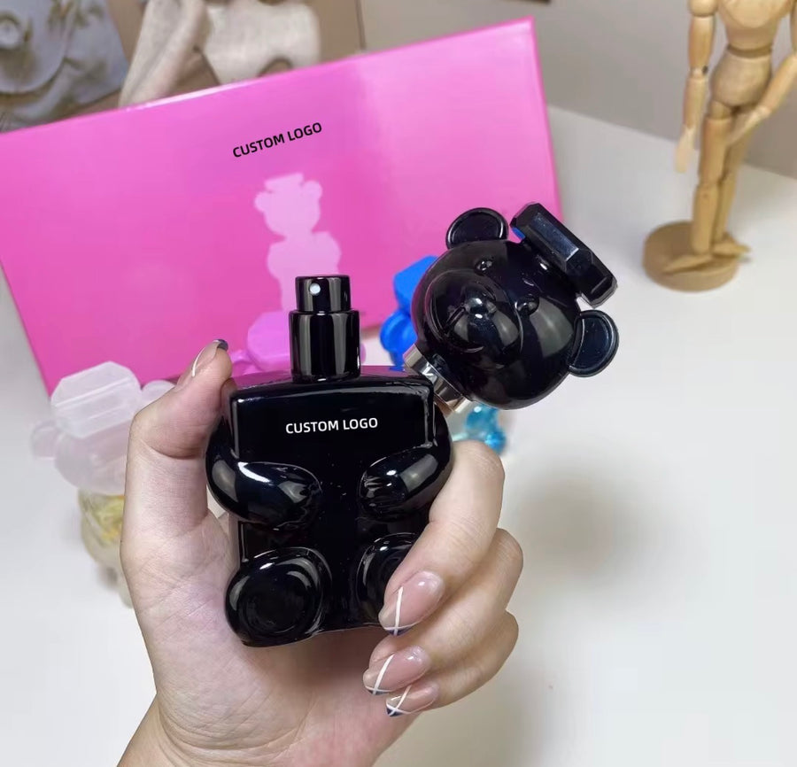 Black bear-shaped perfume bottle with a glossy finish, held in a hand, against a pink box with a bear silhouette.