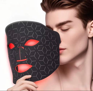 "Black LED light therapy mask with red eye and mouth openings, worn by a person with short brown hair, side view."