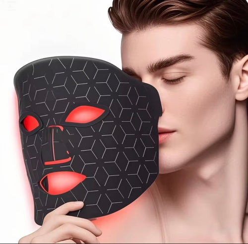 "Black LED light therapy mask with red eye and mouth openings, worn by a person with short brown hair, side view."