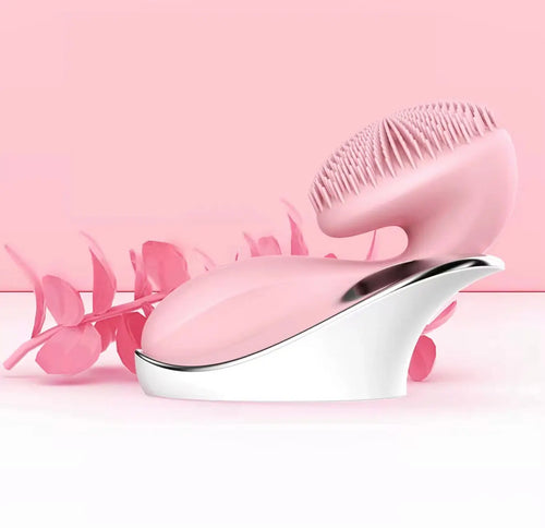"Pink sonic facial cleansing brush with silicone bristles and a curved white base, set against a soft pink background."