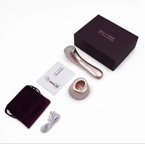 Rose gold beauty device with its charging base, carrying pouch, cable, manual, and a dark purple presentation box on a white background.