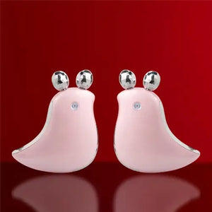 "Pair of pink face sculpting tools shaped like birds, with silver reflective rollers on top, against a red background."