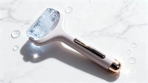 "Beautivana Ice Roller with clear ice head, white handle, and gold accents, resting on a marble surface with water droplets."