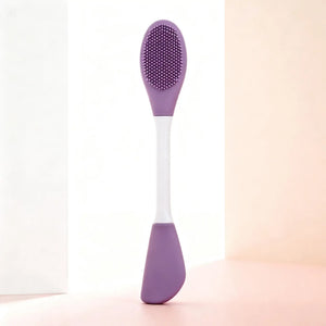 "Double-ended silicone exfoliating brush with a purple textured head and white handle, angled view on soft pastel background.